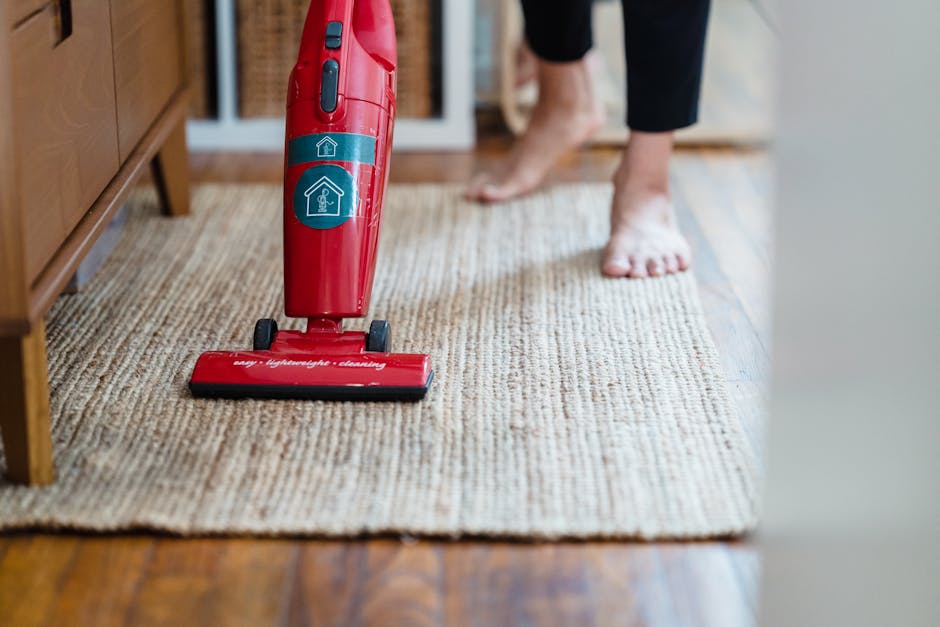 A professional cleaner wearing a full white protective suit, gloves, face mask, and shoe covers is performing deep cleaning or sanitisation on a beige carpet using a steam or extraction cleaning machi